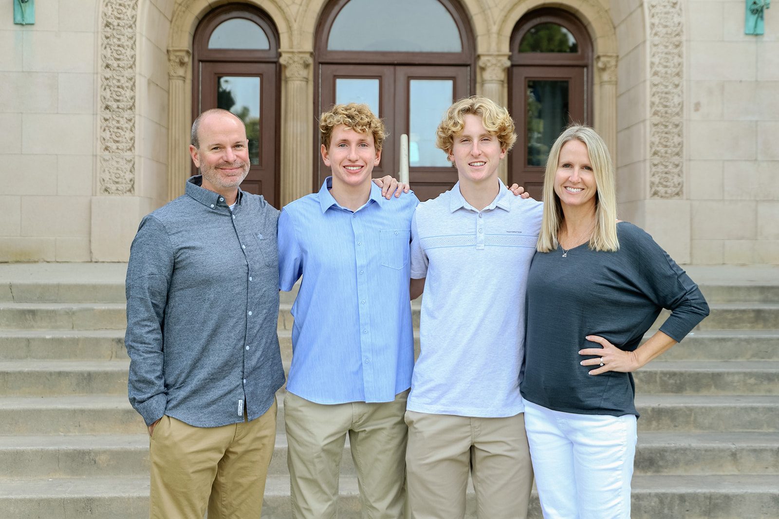 Ryan and Kara Baldino with their two sons on the steps of a brick building, all four standing together