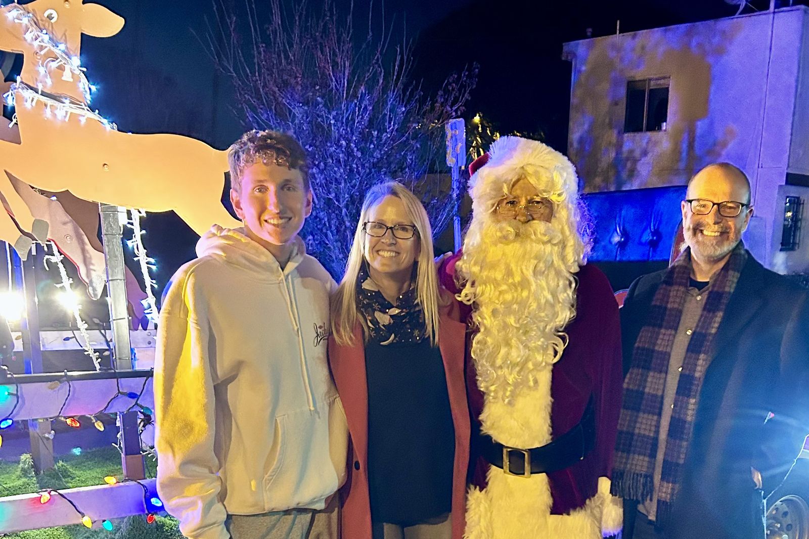 Ryan Baldino with his family beside a lit reindeer display and a costumed Santa on Candy Cane Lane at night.