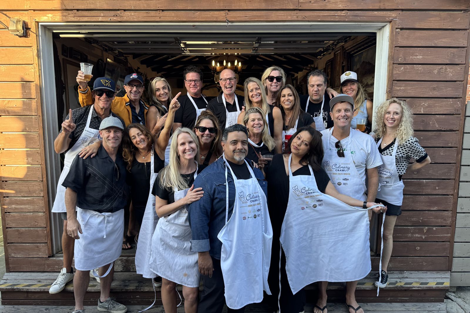 A large group of volunteers in aprons standing together in a wide wooden doorway at a Kiwanis Culinary Crawl.