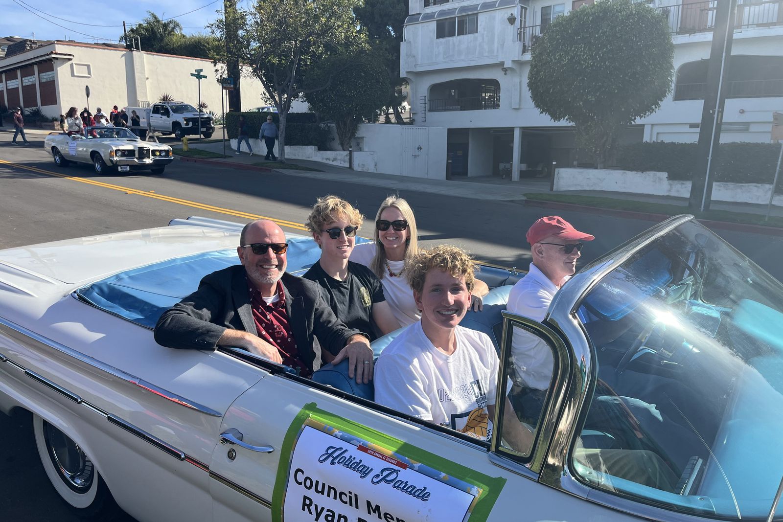 Ryan Baldino and his family riding in a white classic convertible with a Holiday Parade placard on the door.