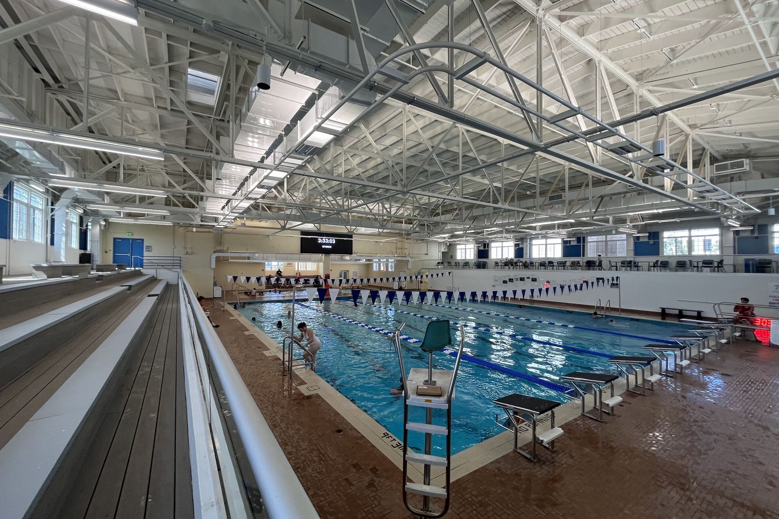 The restored pool at the Urho Saari Swim Stadium, lane lines marked and swimmers in the water beneath the arched roof.
