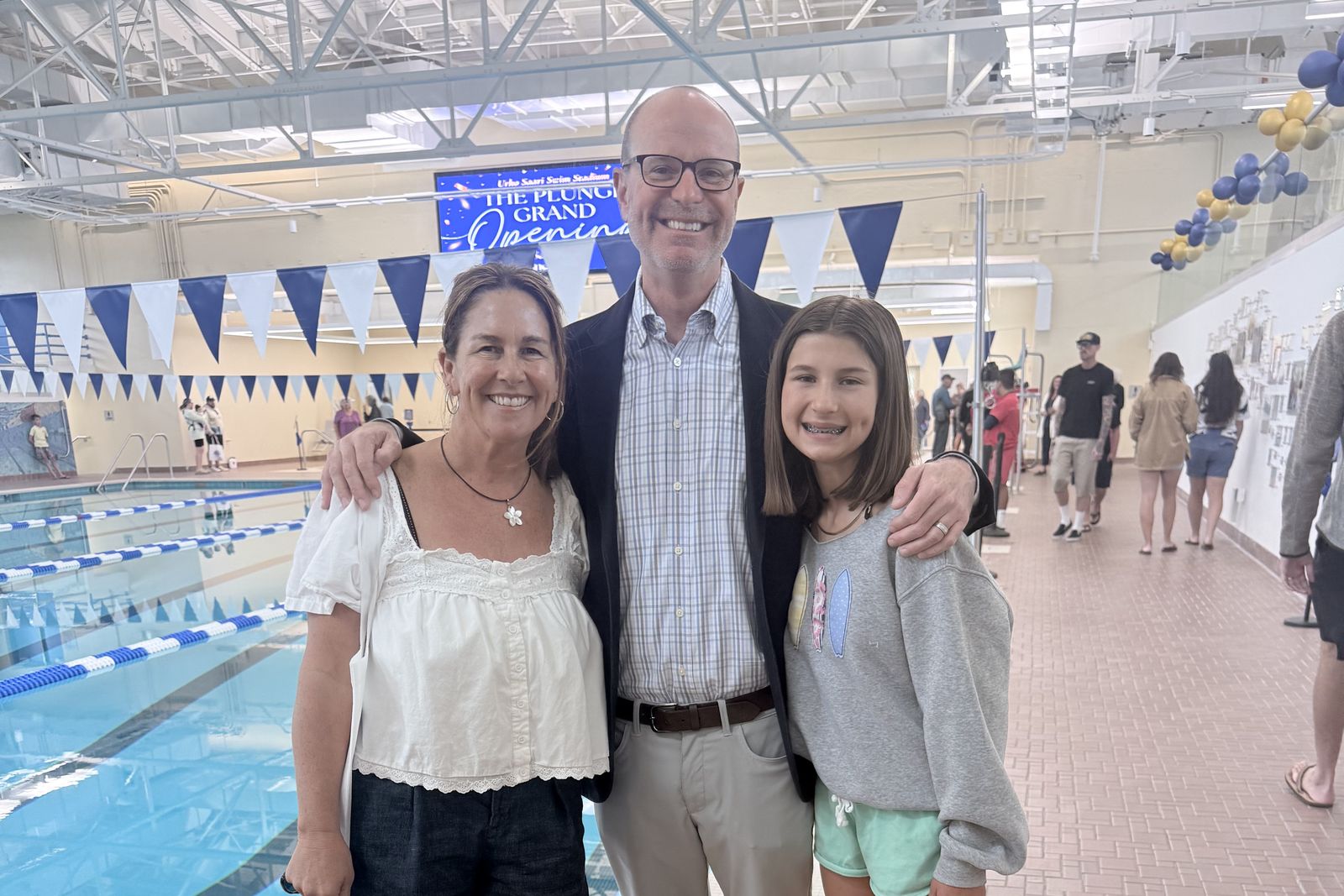 Ryan Baldino with two residents at the reopening of the Urho Saari Swim Stadium, the pool and pennants behind them.