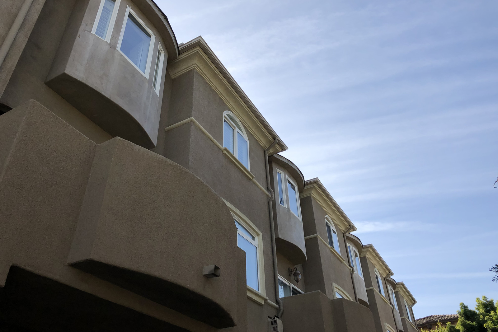 A terrace of three storey townhomes with bay windows and balconies, seen looking up from the pavement against a clear sky